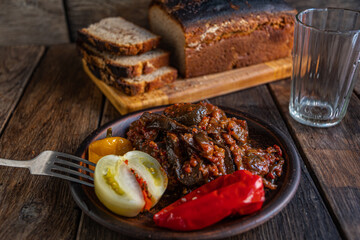 Pickled eggplants, tomato, cucumber, and pepper in earthenware on a wooden table. Homemade pickles. Homebaked bread.