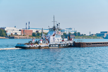 towboat pushes dry bulk cargo barge on the river past the industrial landscape