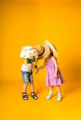 a little boy and a girl in straw hats with flowers kiss on a yellow background with a place for text