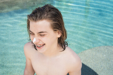 young teen boy with braces laughing in pool with sun block on his nose