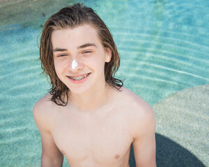 teen boy with long hair smiling showing braces in a pool with sunblock on his nose