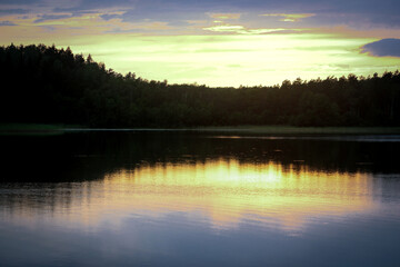 Sunset light over dark forest trees behind lake waters