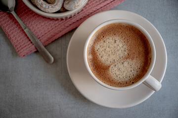 A cup of coffee on a saucer, bagels in a ceramic dish, a karalov-colored kitchen napkin on a gray background.