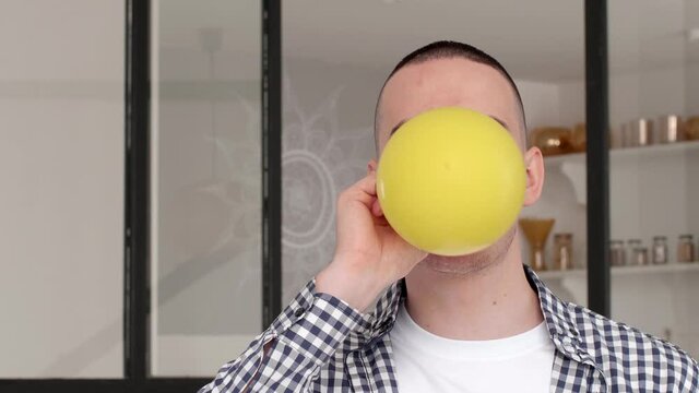 Close-up father man preparing for holiday birthday party, portrait of caucasian millennial guy doing effort inflates balloon inhales air into yellow bubble looking at camera, celebration concept