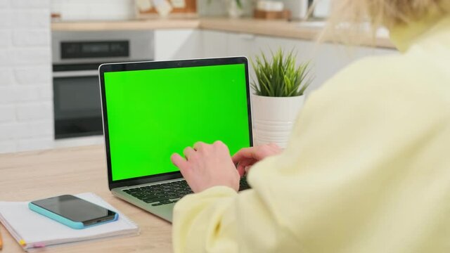 Girl uses green screen chroma key laptop for learning, writes down useful information. distance learning, e-education, e-learning, homeschooling concept. close-up over shoulder POV.