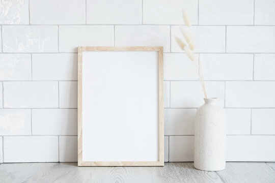 Empty wooden frame mockup and dried flowers in vase on white tiles wall background. Scandinavian interior, home design. Minimal, elegant style.
