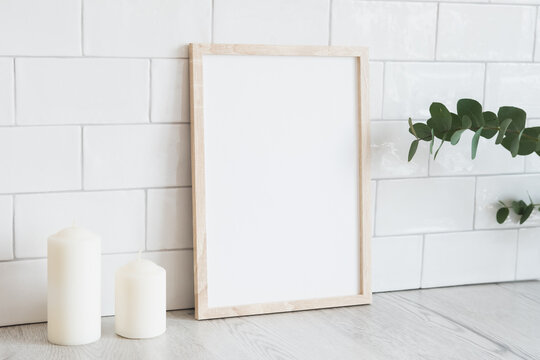 Vertical white picture frame mockup, candles, eucalyptus. Modern home interior, Scandinavian style. White tiles wall background.
