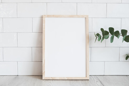 Blank wooden vertical picture frame mockup and eucalyptus on table. Modern home interior, Scandinavian style. White tiles wall background.