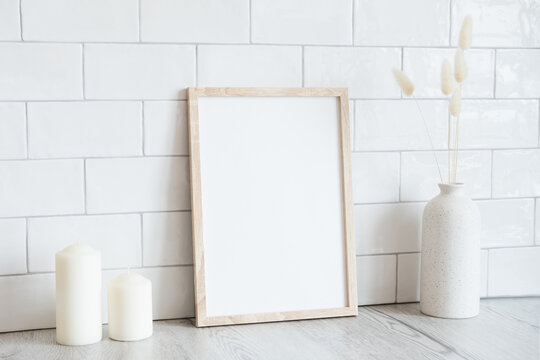 Wooden picture frame mockup, candles, dry flowers in vase on white tiles wall background. Scandinavian interior, home design. Minimal, elegant style.