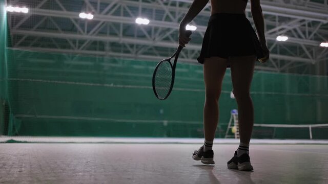 sporty woman is walking on tennis court indoors, throwing ball and catching, rear view, professional sport workout