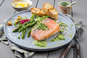 Modern style traditional fried salmon steak with green asparagus and barbecue break served as close-up on a Nordic style plate