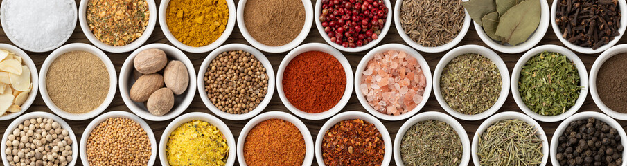 Assorted seasonings and herbs on white bowls. Panorama format