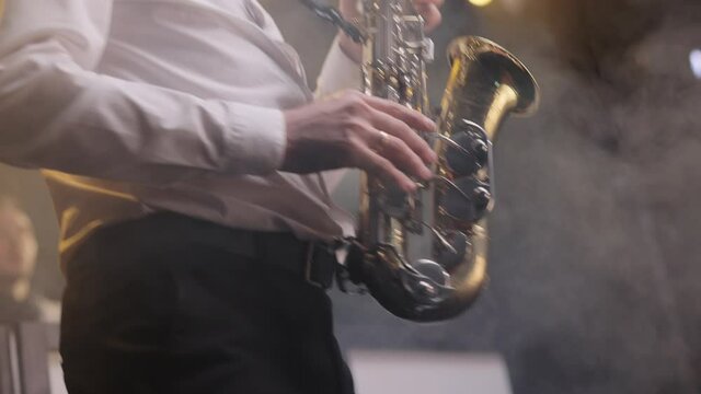 Sax musician player with band at concert. Musical band group playing song, performing on concert musician stage with lights. Saxophone player playing a solo in jazz band, performing on lightened stage