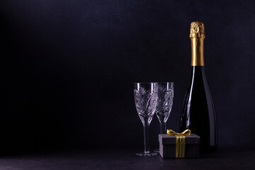 Two crystal glasses and a bottle of alcohol, a box with a surprise on a dark background. Copy space.