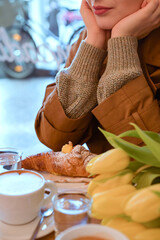 Beautiful young girl in a street cafe with a bouquet of yellow tulips. Breakfast at the coffee shop. Tourism concept. Vintage photo, soft focus. Copy space . close-up