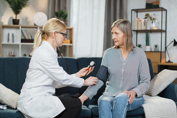 Seniors hypertension concept. Doctor measuring blood pressure to patient at home. Female professional doctor examining elderly old woman patient, measuring arterial blood pressure using tonometer.