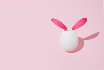 White easter egg with magenta petals on pastel pink background. Minimal artistic card idea.