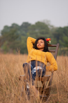 portrait of a beautiful young black woman sitting alone in an open field holding a flower