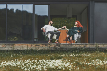 Young married couple sitting on the terrace of modern house in the mountains. 