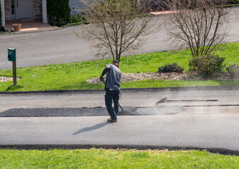 Worker applying a layer of tarmac or extra blacktop to repair damage to asphalt street