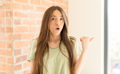 pretty woman looking astonished in disbelief, pointing at object on the side and saying wow,...