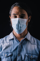 Closeup of a Latino ethnic man wearing a blue medical mask, wearing a blue shirt on a black background. Coronavirus concept. Coronavirus concept