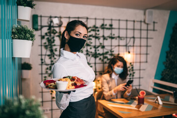 Beautiful young waitress with face protective mask working in restaurant. Coronavirus or Covid-19 concept.