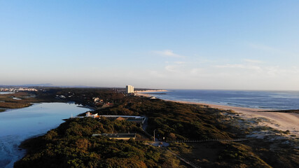 Aerial view of the Northern Litoral Natural Park in Ofir, Esposende, Portugal. Wooden boardwalk and the Ofir Towers in the background. Sea, beach boulders, pebble shore and waves at sunset.