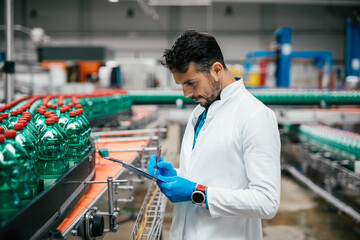 Male worker in bottling factory checking water bottles before shipment. Inspection quality control.