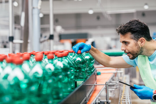 Male worker in bottling factory checking water bottles before shipment. Inspection quality control.