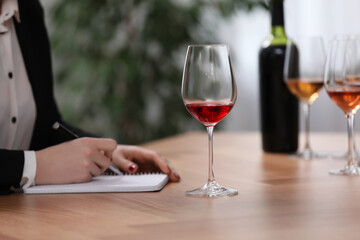 Sommelier making notes during wine tasting at table indoors, closeup
