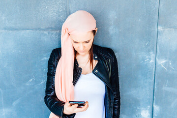 Woman with cancer and pink headscarf checking results on mobile phone with tired face and very...