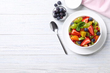 Delicious fresh fruit salad in bowl on white wooden table, flat lay. Space for text