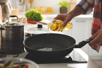 Man pouring cooking oil into frying pan in kitchen, closeup - obrazy, fototapety, plakaty