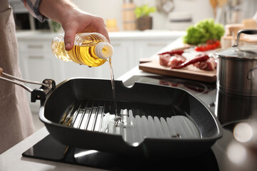 Man pouring cooking oil into frying pan in kitchen, closeup
