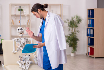 Fototapeta premium Young male doctor suggesting pills to skeleton patient