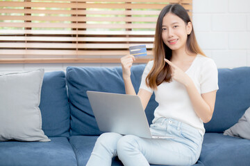 Naklejka premium Young asian woman sit on sofa using laptop computer shopping online with credit card buying to internet, happy girl payment with e-business on couch, purchase and payment, business concept.