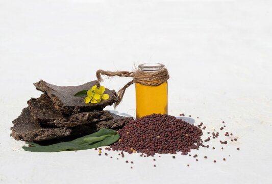Closeup of Mustard Oil in Glass Jar with Black Mustard Seed, Flower and Mustard Cake Isolated on White Background