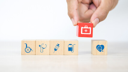 Hand choose medical bag icon on cube wooden toy blocks stacked with other medical symbols concepts of illness treatment and health safety insurance.