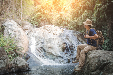 Male hiker with backpack sitting on rock looking at waterfall.