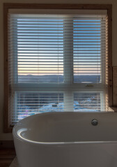 Baignoire en avant d'une fenêtre avec des stores horizontaux sur un coucher de soleil