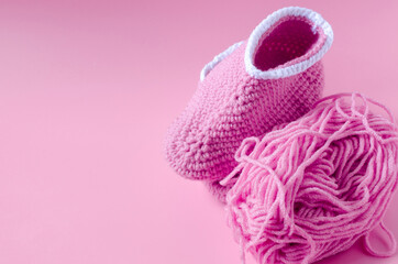 skein of pink yarn with crochet and knitted shoes on a colored background needlework on the background of self-isolation knitting concept