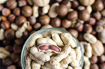 peanuts in a transparent dish on the background of a scattering of different nuts peanuts close up