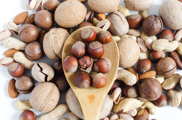 Hazelnuts in a wooden spoon on the background of a scattering of different nuts assorted nuts