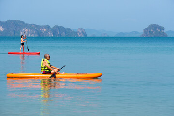 asian senior father playing standing up paddleboard or SUP with young daughter at blue sea on summer vacation. family together concept