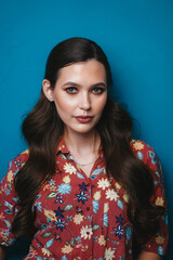 Large portrait of caucasian brunette girl with makeup and styling on a blue wall background. Beauty salon advertising