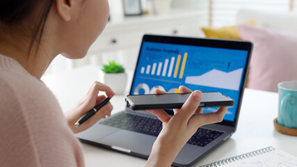 Young happy attractive beautiful asia female talk on mobile phone sit work on desk table at home. Remotely work reskill upskill on distance job or data analysis sale report for business intelligence.