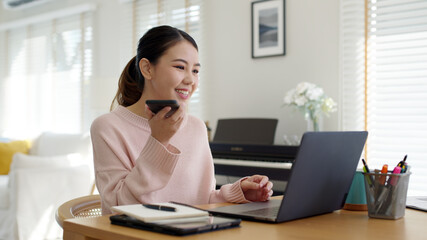 Obraz premium Young happy attractive beautiful asia female staff laugh talk on mobile phone relax comfort sit work on desk table at home. Remotely work on distance job telesale or secretary career for business.