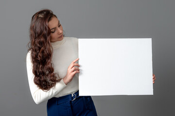 beautiful sensual woman with long curly hair shows a blank banner, isolated on gray, copy space