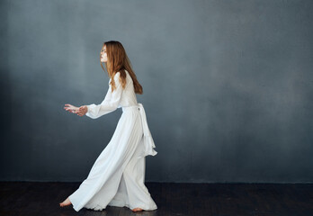 Fototapeta na wymiar A woman in a white dress is dancing on a gray background in full growth red hair model